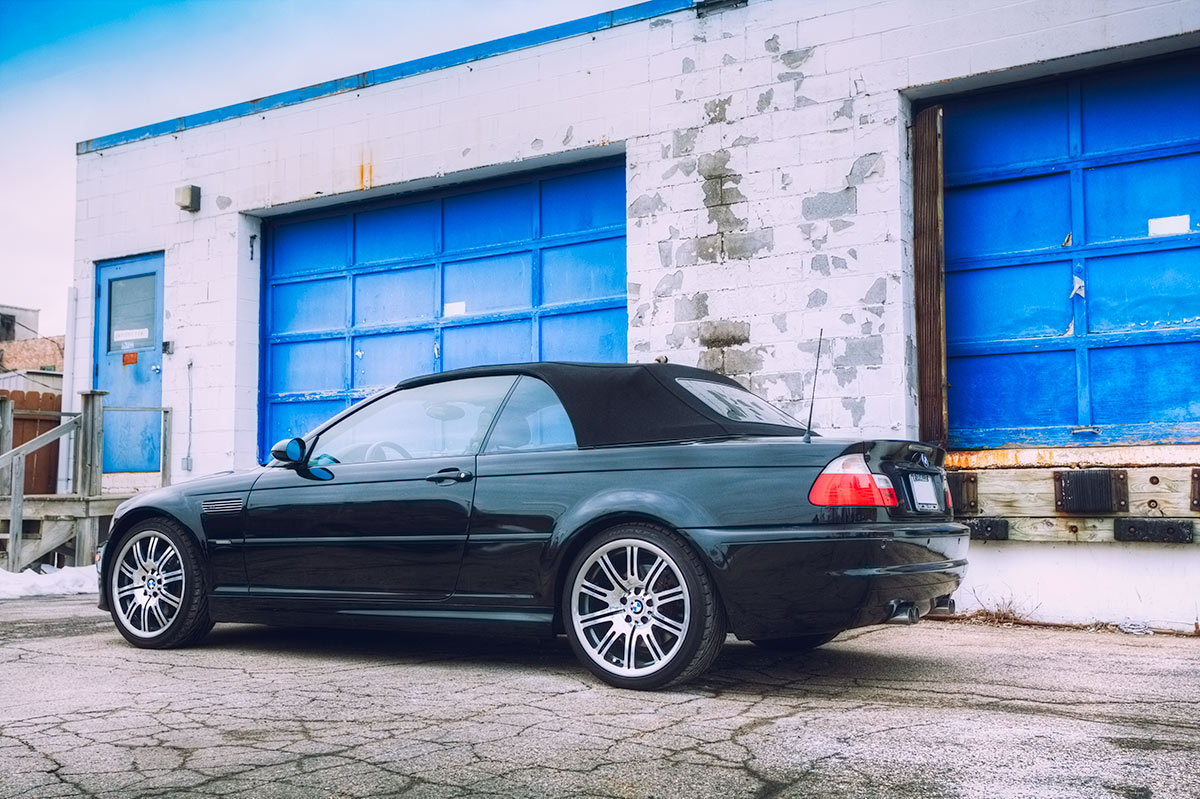 Black 2002 BMW E46 M3 convertible parked near an urban warehouse